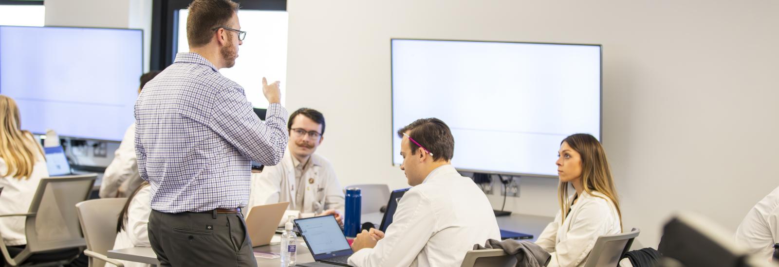 instructor dave matthews talks to a table of pharmd students sitting down