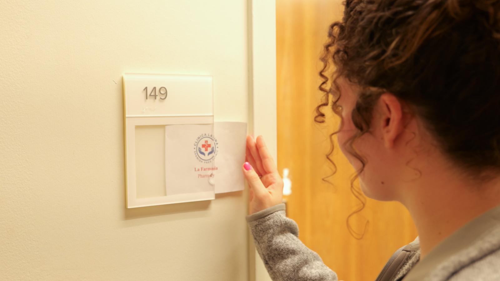 Student pharmacist places the Clinica sign at the pharmacy services' door